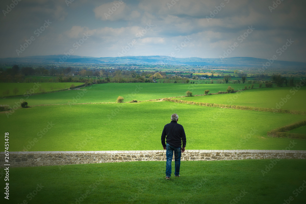 Middle-aged man walking in the field about to jump a wall, a stone fence. Overcome difficulties. Walk facing towards.