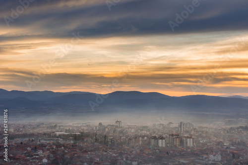 Stunning, soft view of golden sunset sky above scenic cityscape covered by haze and mist