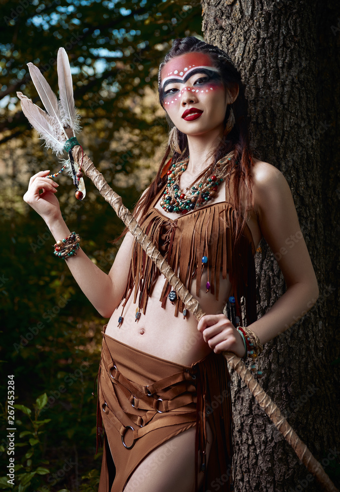 Outdoor portrait of beautiful young shamaness (witch doctor) with stick.  Cute smiling shaman (sorceress) stands at tree in forest Stock Photo |  Adobe Stock
