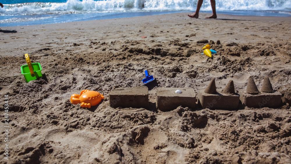 Sand castle on the beach with colorful toys and a small bucket Sand castle on the beach with colorful toys and a small bucket