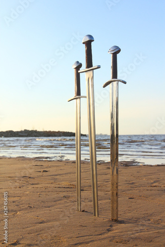 Three swords in sand of battlefield