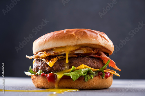 Tasty grilled beef burger with fried bacon and eggs, cheese, tomatoes and lettuce.