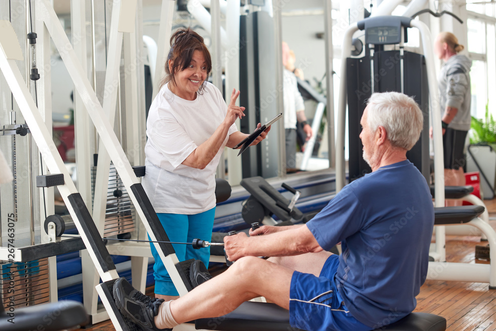 Senior people exercising at gym. Elderly woman using digital tablet at fitness club. People, sport, modern technology and lifestyle concept. Senior people exercising at gym. Elderly woman using digital tablet at fitness club. People, sport, modern technology and lifestyle concept.