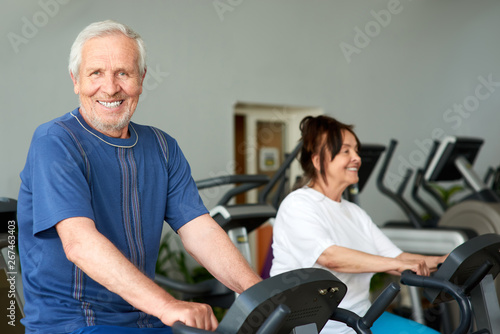 Happy elderly man working out in gym. Smiling caucasian pensioner looking at camera while training at gym. Sport and seniors.