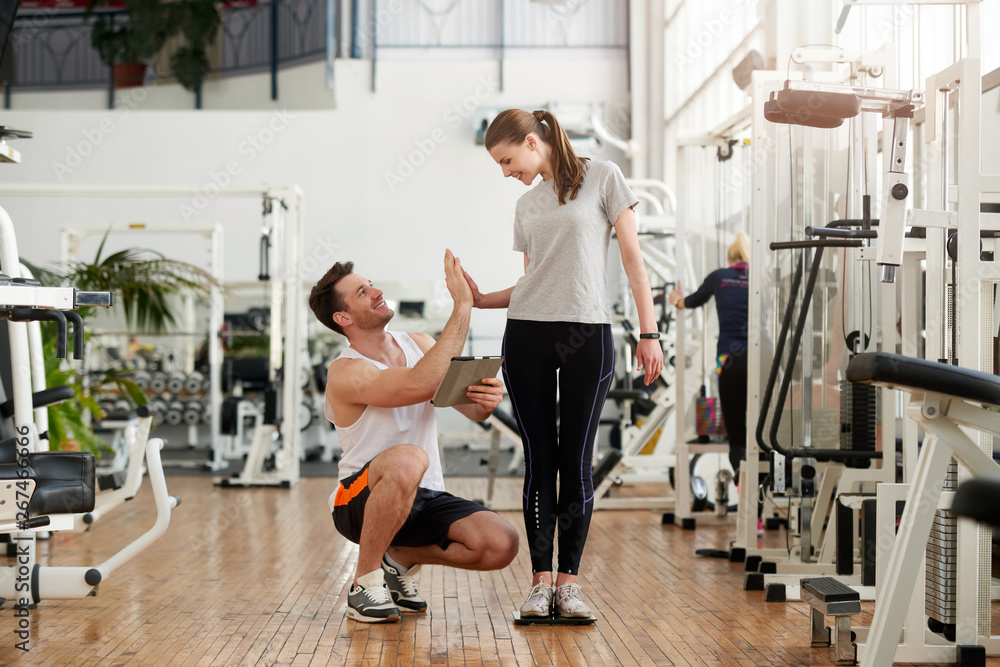 Happy woman celebrating weight loss. Woman with personal trainer give high five. Personal fitness achievement concept.