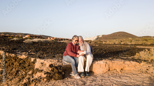 Relaxing moment for a senior couple during an excursion on the arid land of south Tenerife.  Mountains on the background. Two people looking at the mobile phone.