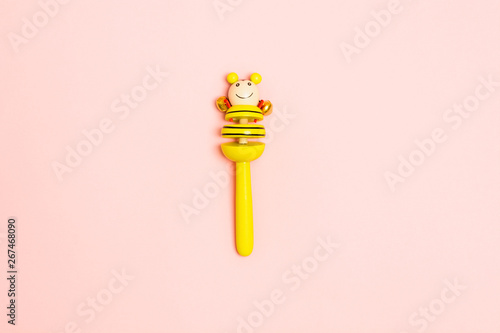 Yellow wooden baby rattle with bells over pink background. Mock up. Copy space. Flat lay style photo