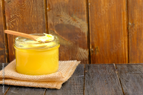 Ghee butter in a jar on wooden background, copy space