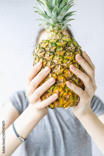 Girl holding a pineapple in front of her face over white background. Raw eating concept Summer and vacantion time.
