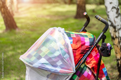 Child in stroller covered with protective net during walk. Baby carriage with anti-mosquito white cover. Midge protection for children during outdoor walking season photo