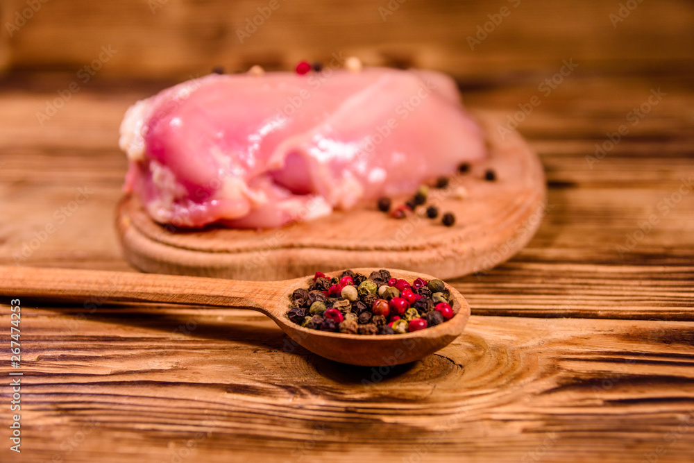 Cutting board with raw chicken fillet and spoon with different spices on wooden table