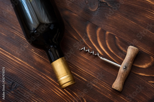 A dark bottle of wine next to a corkscrew on a wooden background.
