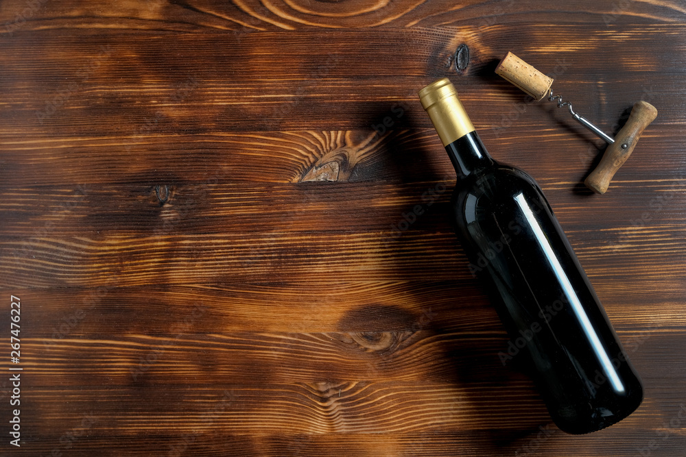 A dark bottle of wine next to a corkscrew and a twisted cork at the left side on a wooden background.