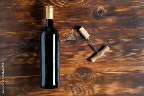 A dark bottle of wine next to a corkscrew and a twisted cork at the center on a wooden background.