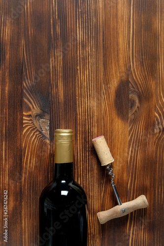 A dark bottle of wine next to a corkscrew and a twisted cork at the center side on a wooden background.
