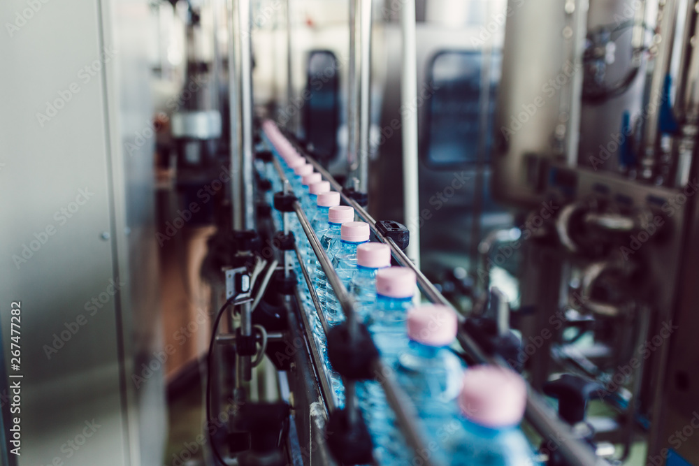 Fototapeta premium Bottling plant - Water bottling line for processing and bottling carbonated water into bottles. Selective focus.