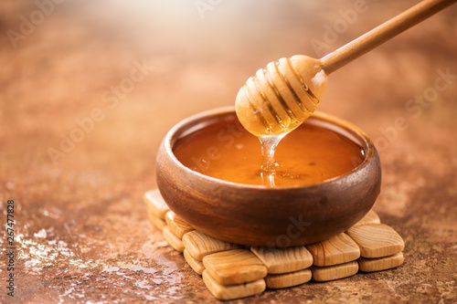 Honey dripping from honey dipper in wooden bowl. Healthy organic thick honey pouring from the wooden honey spoon closeup