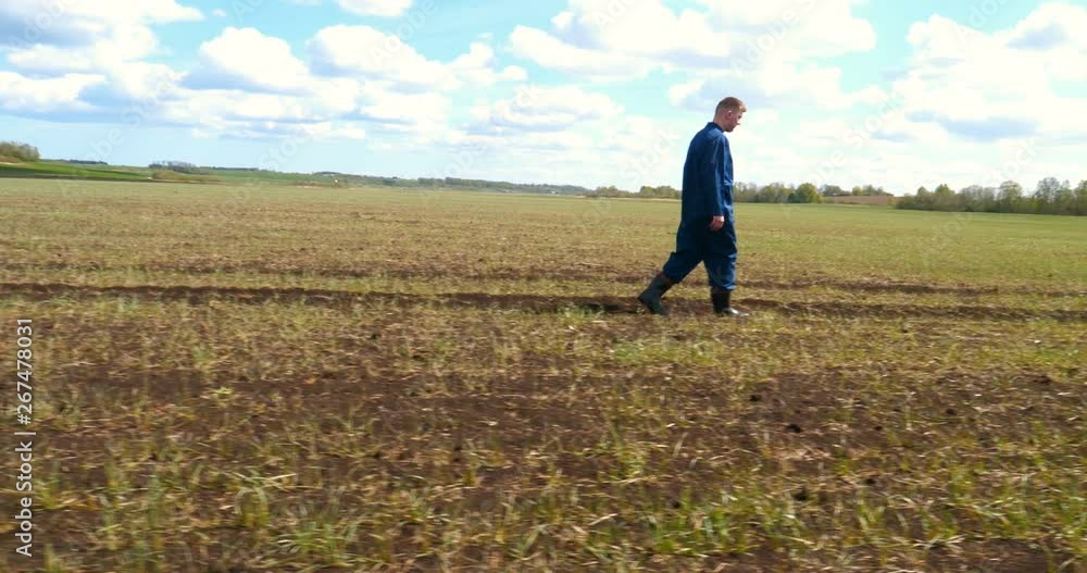 A young guy (man), a farmer in a working uniform, walks across a field in rubber boots. Concept of: Freedom, Rubber boots, Lifestyle, Farmer, Heaven, Slow Shooting, Fields. A young guy (man), a farmer in a working uniform, walks across a field in rubber boots. Concept of: Freedom, Rubber boots, Lifestyle, Farmer, Heaven, Slow Shooting, Fields.