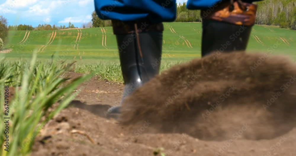 A young guy (man), a farmer in a working uniform, walks across a field in rubber boots. Concept of: Freedom, Rubber boots, Lifestyle, Farmer, Heaven, Slow Shooting, Fields. A young guy (man), a farmer in a working uniform, walks across a field in rubber boots. Concept of: Freedom, Rubber boots, Lifestyle, Farmer, Heaven, Slow Shooting, Fields.