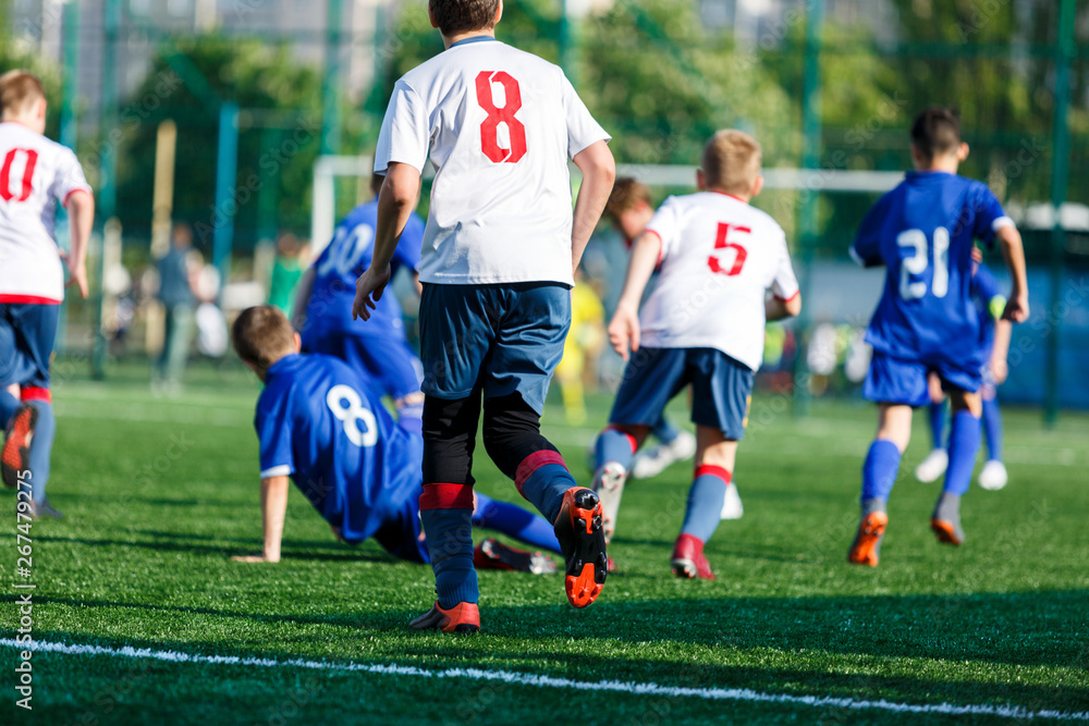 Junior football match. Boys in blue white sportswear play soccer match on football pitch. Football stadium, grass field at the background Soccer for young players. Training, sport, activity outdoor Junior football match. Boys in blue white sportswear play soccer match on football pitch. Football stadium, grass field at the background Soccer for young players. Training, sport, activity outdoor