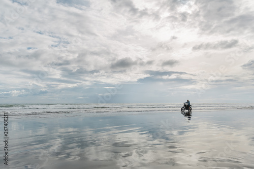 Man in cap riding motorcycle on beach. Moto cross dirtbiker on beach sunset on Bali. Young hipster male enjoying freedom and active lifestyle, having fun on a bikers tour.