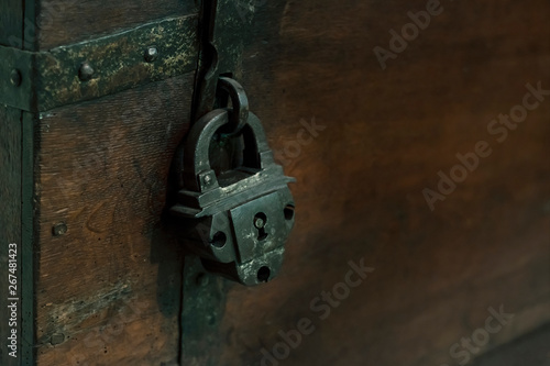 Reliable metal lock of the old design locks the bolt of an antique wooden chest, close-up, moonlight.