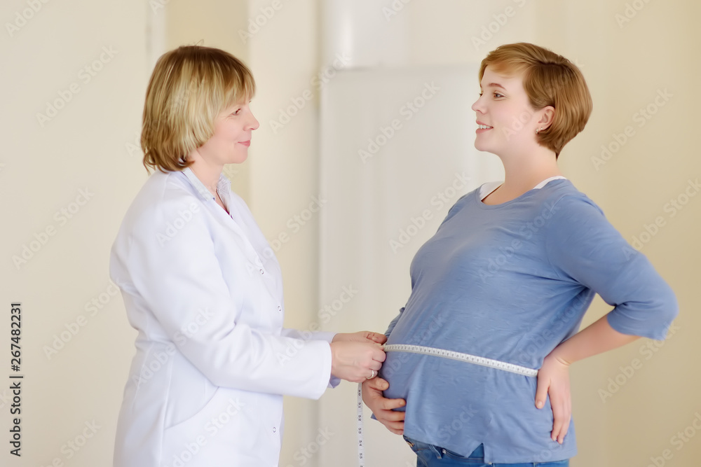 Obraz premium Gynecologist doctor measures with centimeter tape of a pregnant woman. Medical insurance childbearing. Family doctor for gestation. Maternity leave.