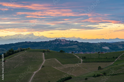 The village and castle of Magliano Alfieri, sunset light with alps mountain background. Langhe vineyards in Piedmont, Italy