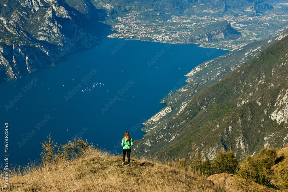 A beautiful woman admiring the beautiful Lake Garda from Monte Baldo, Panorama of the gorgeous Garda lake surrounded by mountains