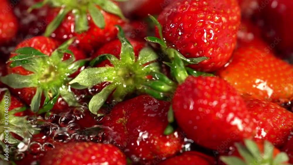 Strawberry watering and fermented. Close up of crop of picked freshly red berry and green leaves in cold pouring water for canning with chaotic motion. Strawberry watering and fermented. Close up of crop of picked freshly red berry and green leaves in cold pouring water for canning with chaotic motion.