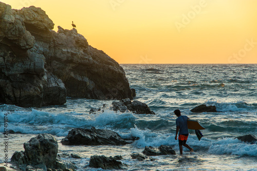 Bodyboardeur en couché de soleil avec un pélican sur une falaise en fond, Puerto Escondido, Oaxaca, Mexique. photo