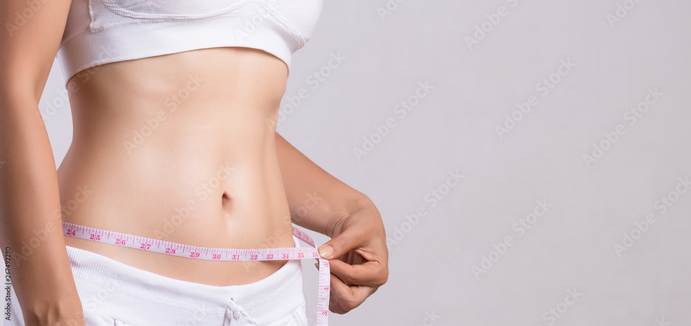 Photo of Young slim woman measuring her waist with a tape