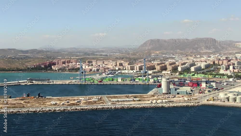 Alicante, Spain sea port seen from drone overhead looking out to sea. Trucks and activity around the docks. Sky filled with sunshine and blue, calm ocean. Buildings near the waterfront. Alicante, Spain sea port seen from drone overhead looking out to sea. Trucks and activity around the docks. Sky filled with sunshine and blue, calm ocean. Buildings near the waterfront.