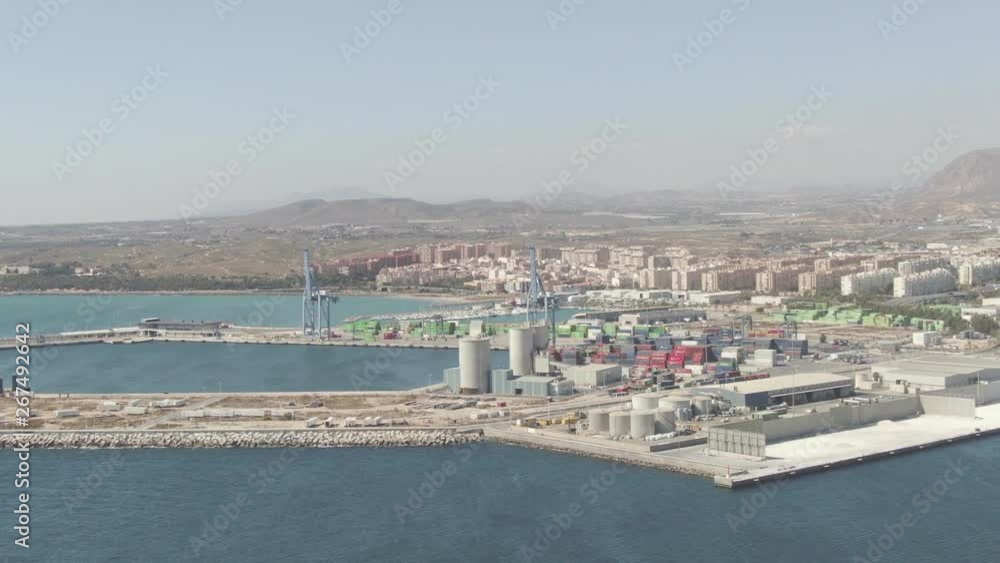 Drone flying high over the ocean looking back at Alicante, Spain with the seaport in the foreground and city beyond. Mountains rise up from the brown landscape in the distance. Aerial view. Ungraded. Drone flying high over the ocean looking back at Alicante, Spain with the seaport in the foreground and city beyond. Mountains rise up from the brown landscape in the distance. Aerial view. Ungraded.