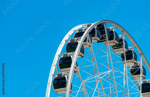 Closeup modern Ferris wheel against blue sky and white clouds. Ferris wheel at funfair for entertainment and recreation on holiday. Modern construction of Ferris wheel in amusement. Fun festival.