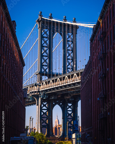 Fototapeta Naklejka Na Ścianę i Meble -  Manhattan bridge seen from a narrow alley enclosed by two brick buildings on a sunny day in summer