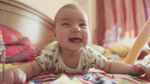 a newborn baby lies on his stomach and learns to hold his head. The kid looks at the camera photo