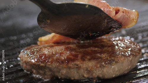 Hamburger meat grilling with bacon slice on top photo