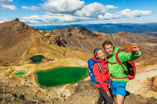 New Zealand Tongariro Alpine Crossing Hiking tourists couple selfie at Emerald Lakes. Happy backpackers tramping taking phone photo of themselves at volcanic mountains. Tramping track of New Zealand. photo