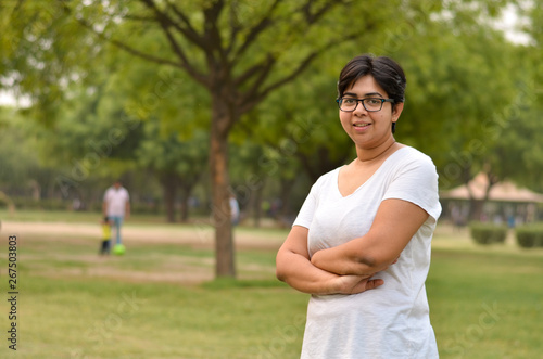 Smart Indian woman standing, posing for the camera with hands crossed in a park wearing white in summers in Delhi, India