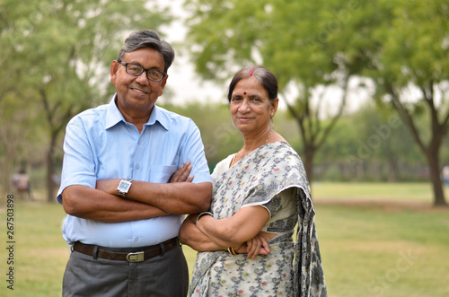 Happy looking retired senior Indian man and woman couple smiling and posing with hands crossed in a park outdoor setting in Delhi, India. Concept love