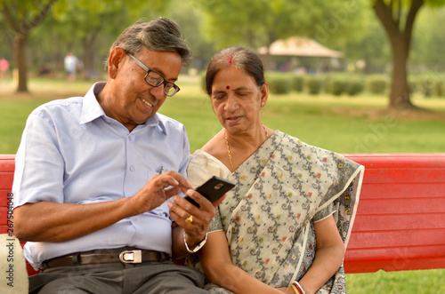 Wallpaper Mural Senior couple sitting in park looking at  their smart phone and laughing in Delhi, India Torontodigital.ca
