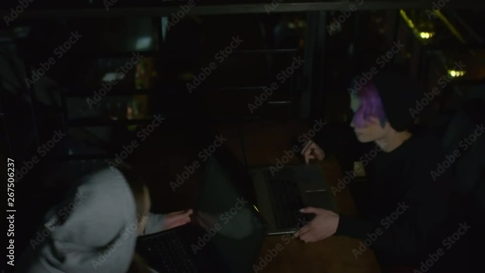 High angle view of two young Caucasian women in hoodie sitting down at table in front of each other, putting laptops on it and starting typing on keyboards High angle view of two young Caucasian women in hoodie sitting down at table in front of each other, putting laptops on it and starting typing on keyboards