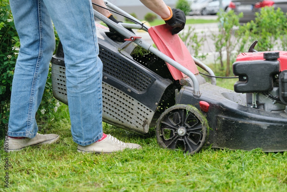 Gardener woman legs mowing grass with lawnmower, city courtyard of an apartment building Gardener woman legs mowing grass with lawnmower, city courtyard of an apartment building