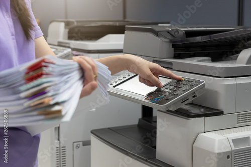 Bussinesswoman using copier machine to copy heap of paperwork in office. photo