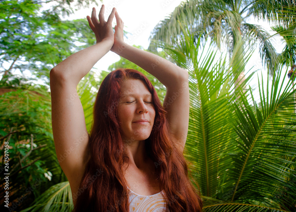 natural portrait of young happy and attractive woman with beautiful long red hair doing yoga meditation exercise at amazing tropical jungle background in healthy lifestyle and harmony natural portrait of young happy and attractive woman with beautiful long red hair doing yoga meditation exercise at amazing tropical jungle background in healthy lifestyle and harmony