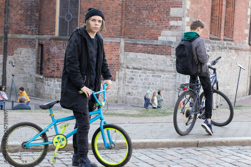 European teenager with dreadlocks in a black hat and black clothes with a bicycle on the background of the old town