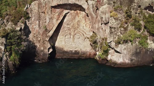 Drone shot of a large Maori rock carving on blue water