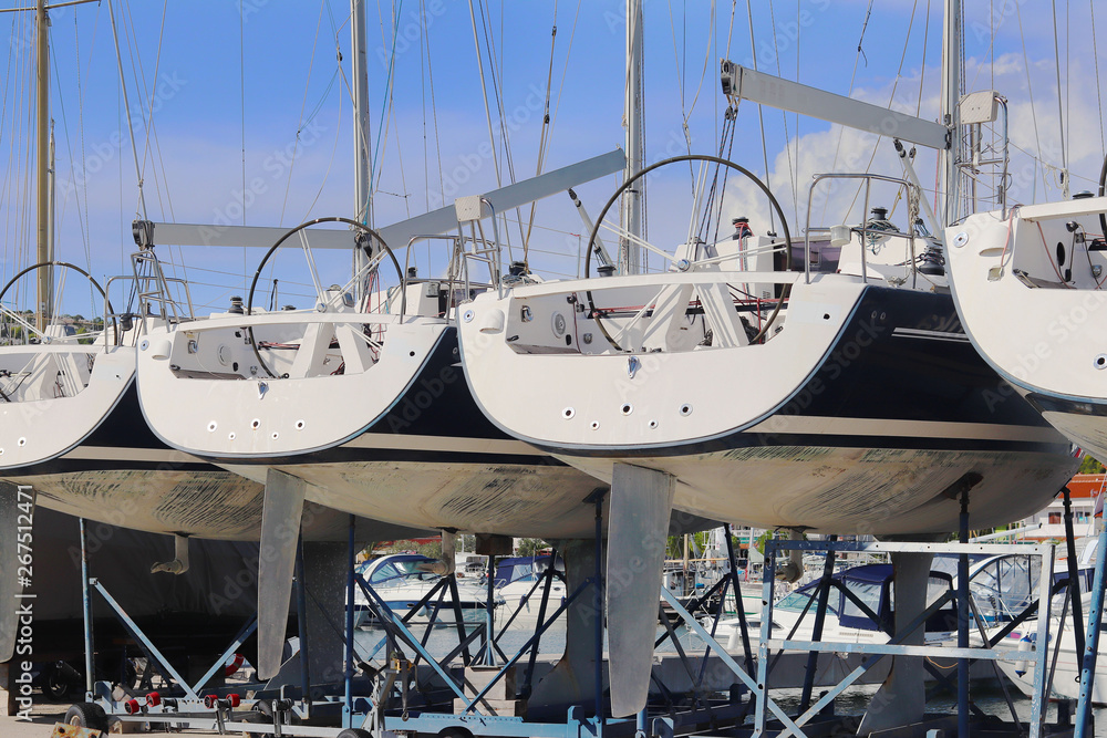Same yachts stand in a row on the dry parking in the marina on a sunny summer day. Device sailing vessel below the waterline. Stern sports boat. Mediterranean city. Preparing for the sailing charter