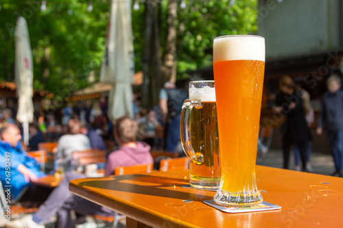 A wheat beer and a pils are standing on a table in a beer garden